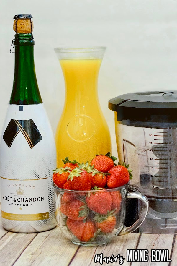 Meauring cup full of strawberries next to champagne and bottle of orange juice