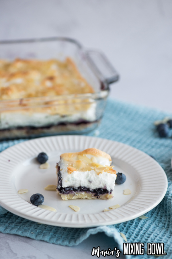 blueberry meringue square on a white dish on a blue towel
