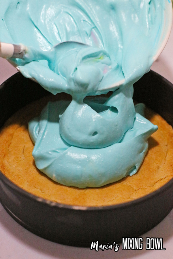 Blue cheesecake batter being poured over cheesecake in springform pan