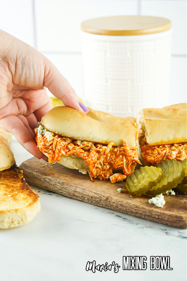 Slow Cooker Buffalo Chicken Cheesesteaks on board with pickles white canister in background