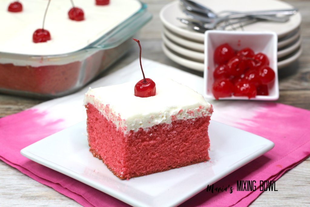 Slice of cherry sheet cake on plate with more cake in background