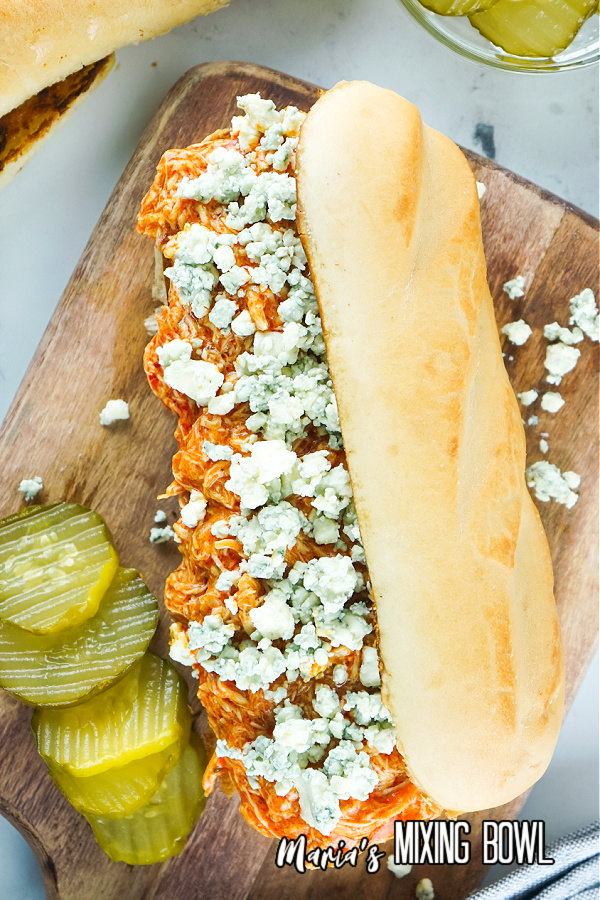 Slow Cooker Buffalo Chicken Cheesesteaks with pickles, blue cheese crumbles on board