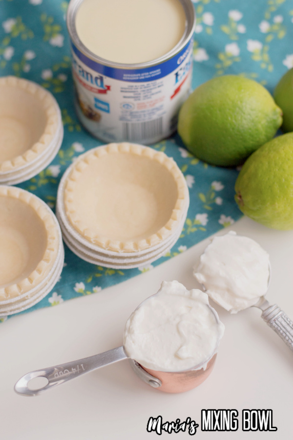 Mini pie crusts next to scooper filled with lime filling