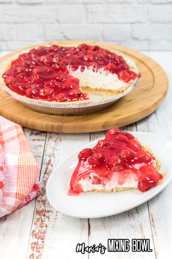 Slice of no-bake cherry cheesecake on plate in front of cheese cake in pan
