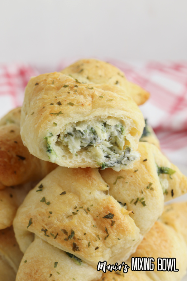 Spinach artichoke crescent rolls stacked atop one another with bite taken out of top roll