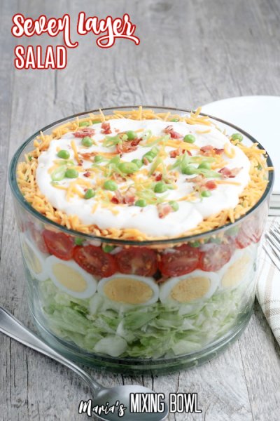 Seven Layer Salad on a grey table with white plates and napkins