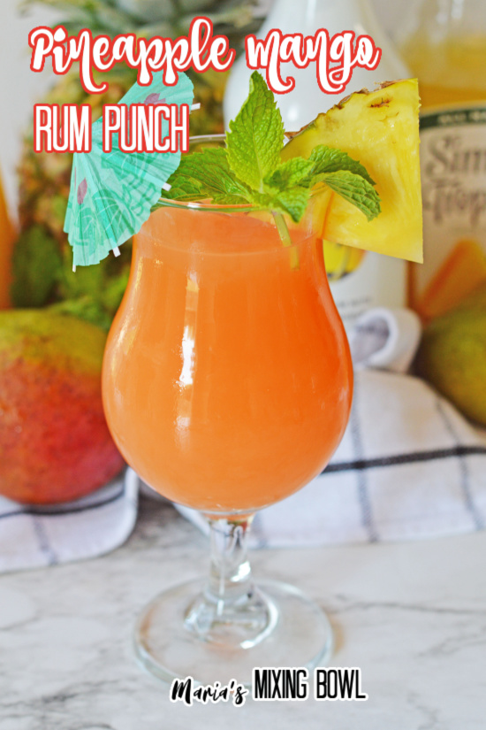 Glass of pineapple rum punch garnished with umbrella, mint, and pineapple wedge