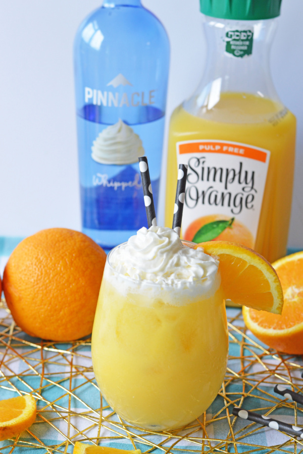 Orange creamsicle alcoholic drink with orange juice and vodka bottles in background