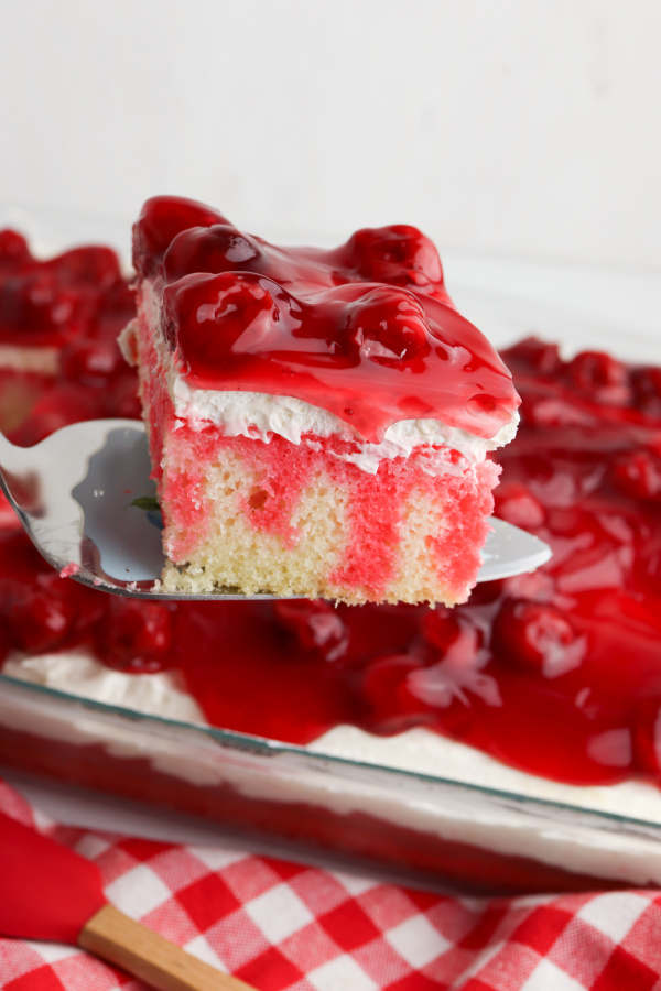 Closeup shot of slice of cherry cheesecake poke cake with more poke cake in background