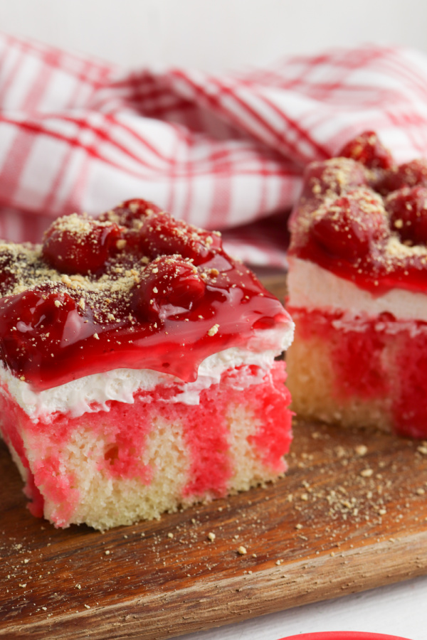 Closeup shot of two pieces of cherry cheesecake poke cake on board