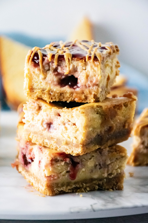 Three peanut butter and jelly cheesecake bars stacked atop one another