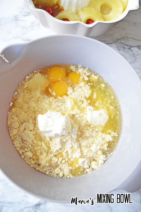 cake mix in white bowl, pineapple and cherries in pan