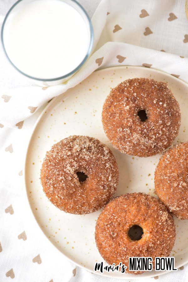Overhead shot of plateful of baked apple cinnamon donuts next to glass of milk