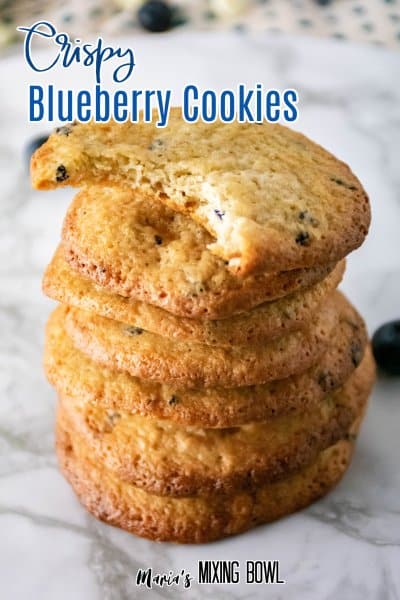 stack of crispy blueberry cookies on a marble counter with top one with a bite missing