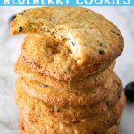 stack of crispy blueberry cookies on a marble counter with top one with a bite missing with text for pinterest