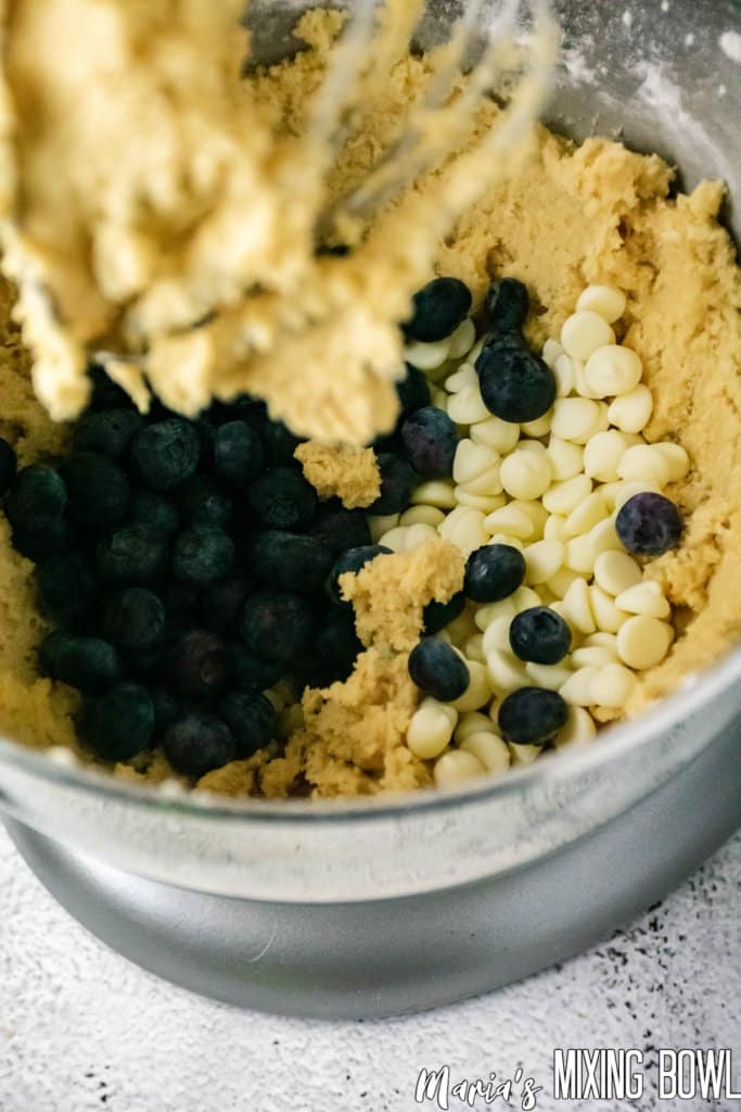 blueberries and white chooclate chips being added to dough in a mixer