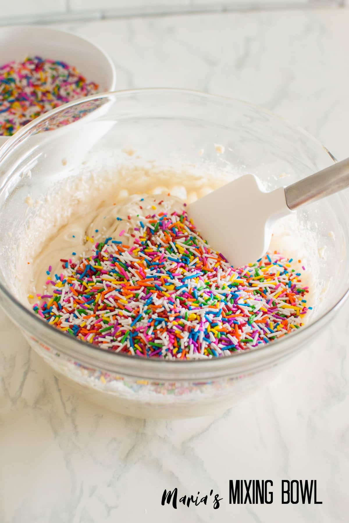 sprinkles being mixed into cream cheese in a glass bowl