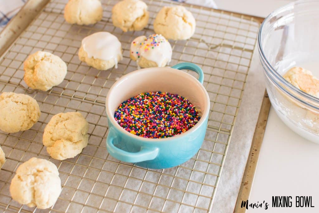 cookies being iced and sprinkles on a baking rack