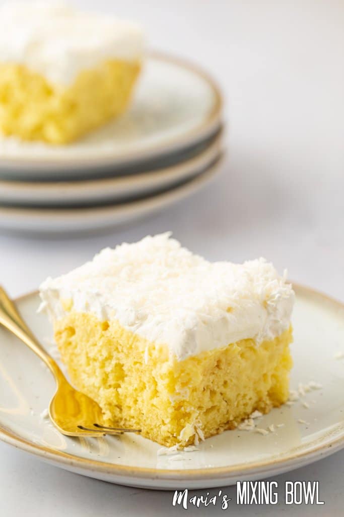 slice of pineapple coconut poke cake on a white and gold plate