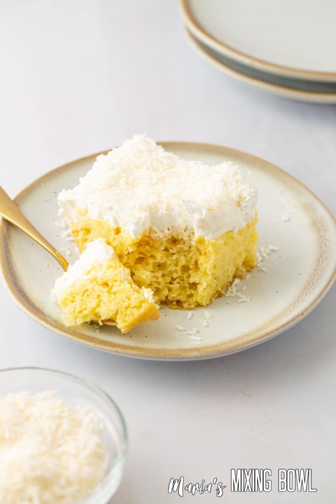 slice of pineapple coconut poke cake on a white and gold plate with bite on a fork