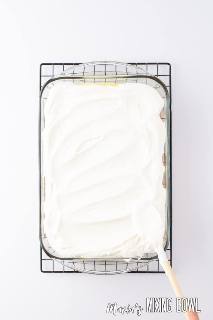 whipped topping being spread on a cake in a glass baking dish