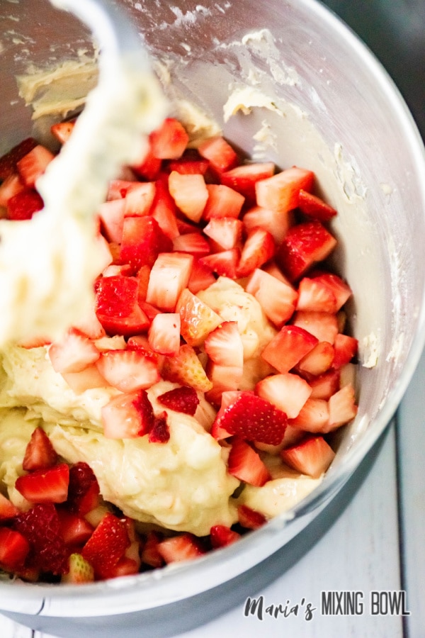 diced strawberries being mixed into dough in a stand mixer