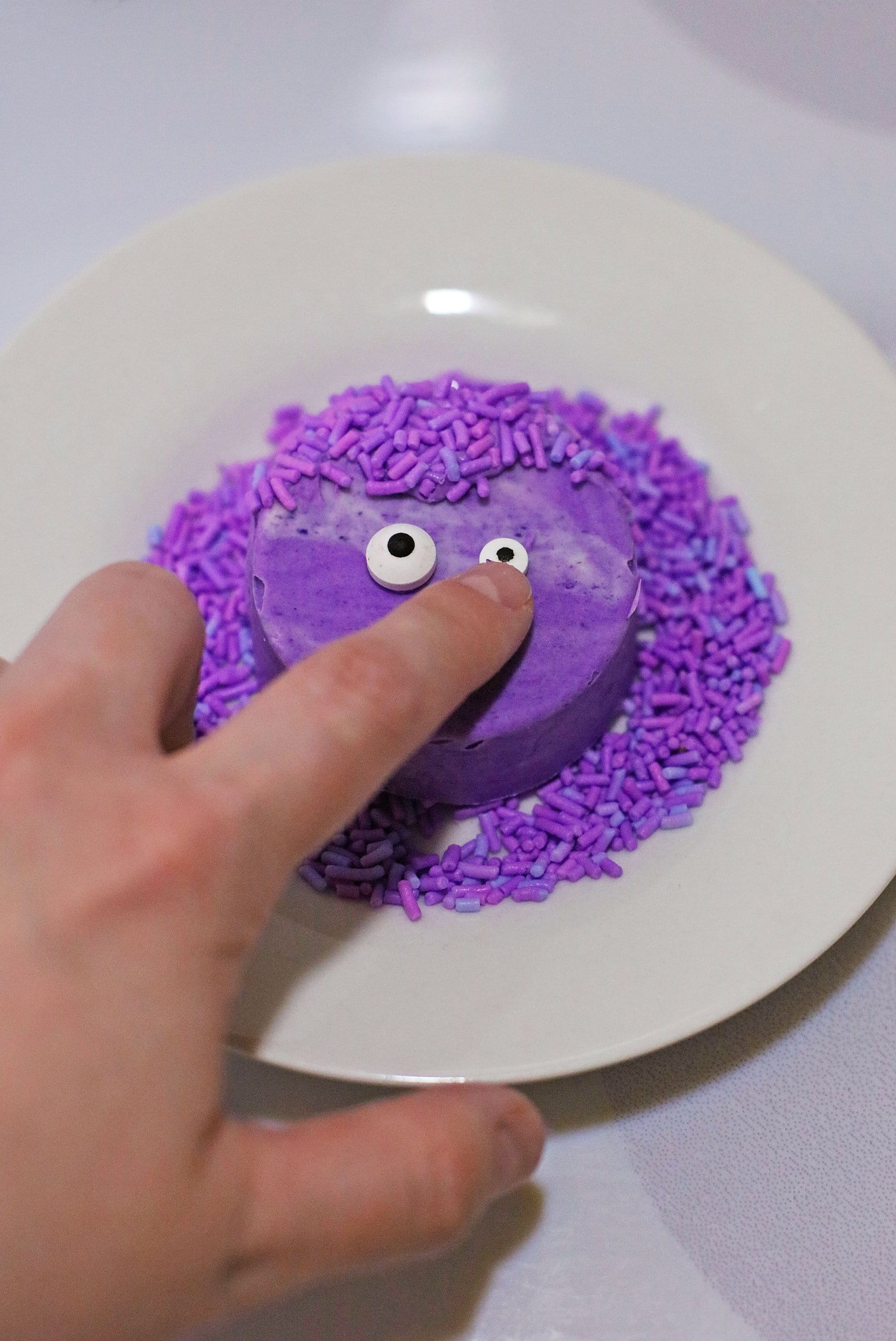 candy eyeballs being added to a purple dipped cookie