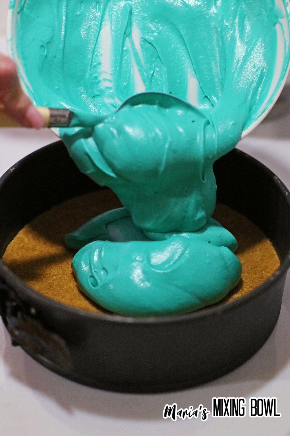 blue batter being poured over a crust in a springform pan
