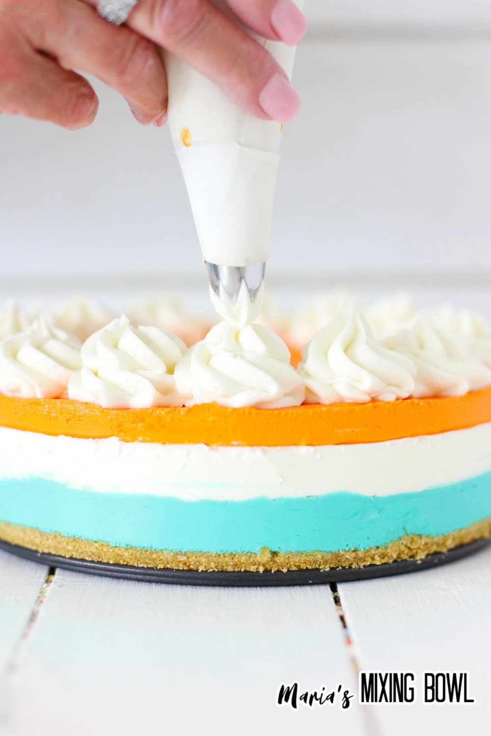 whipped cream being piped on top of the orange and blue cake