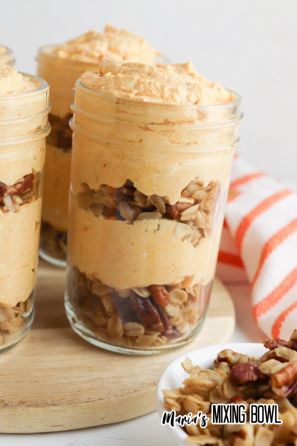 four pumpkin cheesecake parfaits on a wooden cutting board
