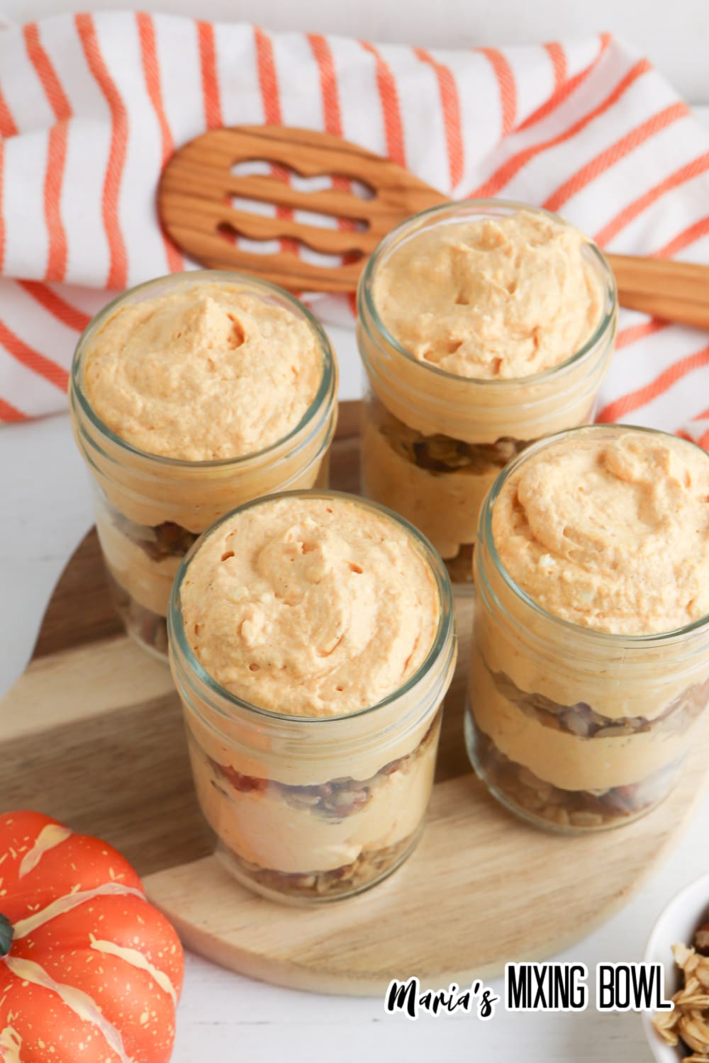 four pumpkin cheesecake parfaits on a wooden cutting board