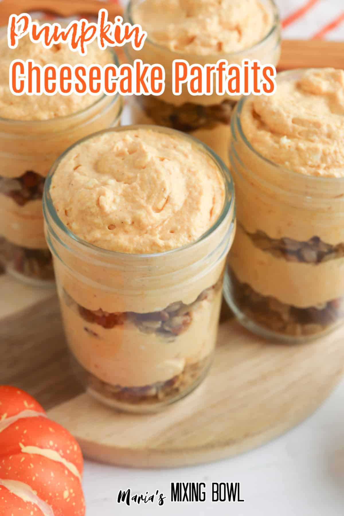 four pumpkin cheesecake parfaits on a wooden cutting board