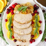 sliced turkey breast on a white plate garnished with oranges and cranberries