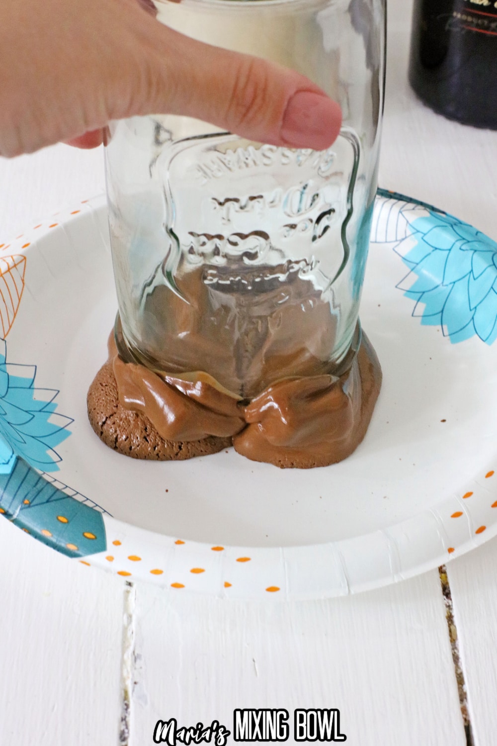 melted chocolate on a paper plate with a mason jar being dipped into it