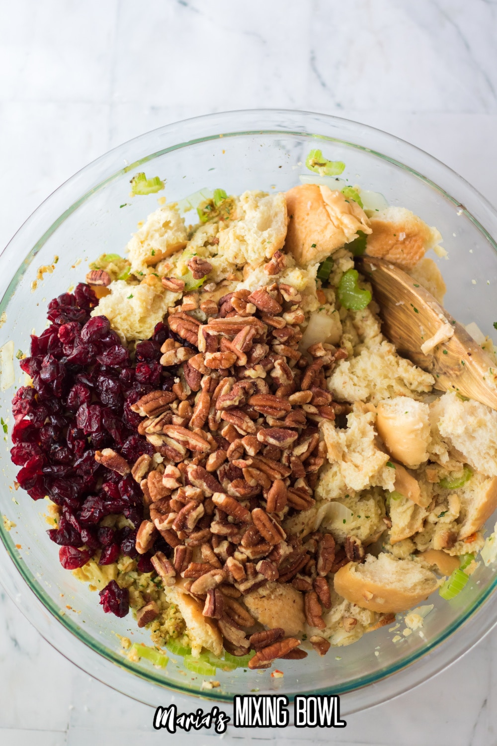 pecans, bread pieces, cranberries and cooked vegtables in a glass mixing bowl
