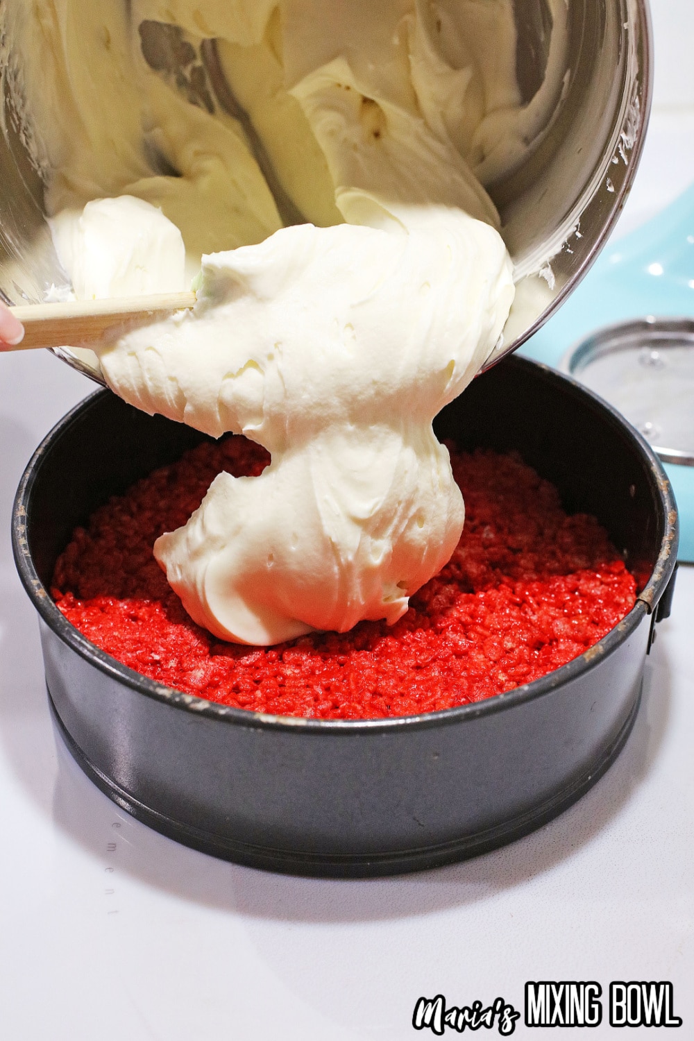 cheesecake being poured on a red rice krispies layer in a springform pan