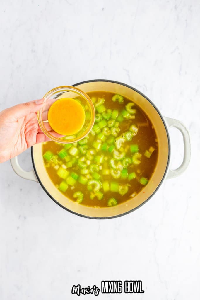 celery, onions, and chicken paste being added to a white dutch oven filled with broth