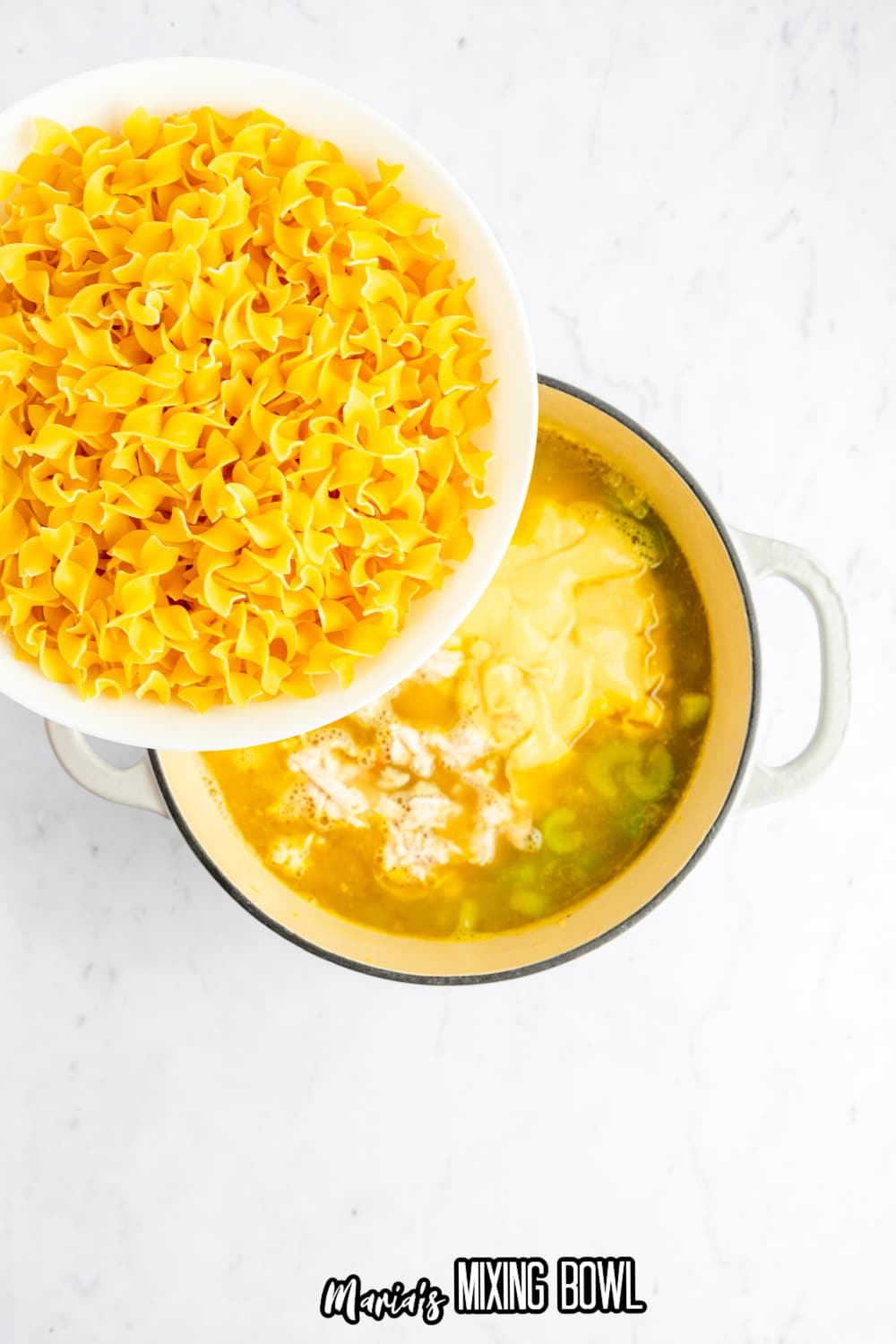 noodles being added to broth in a white dutch oven