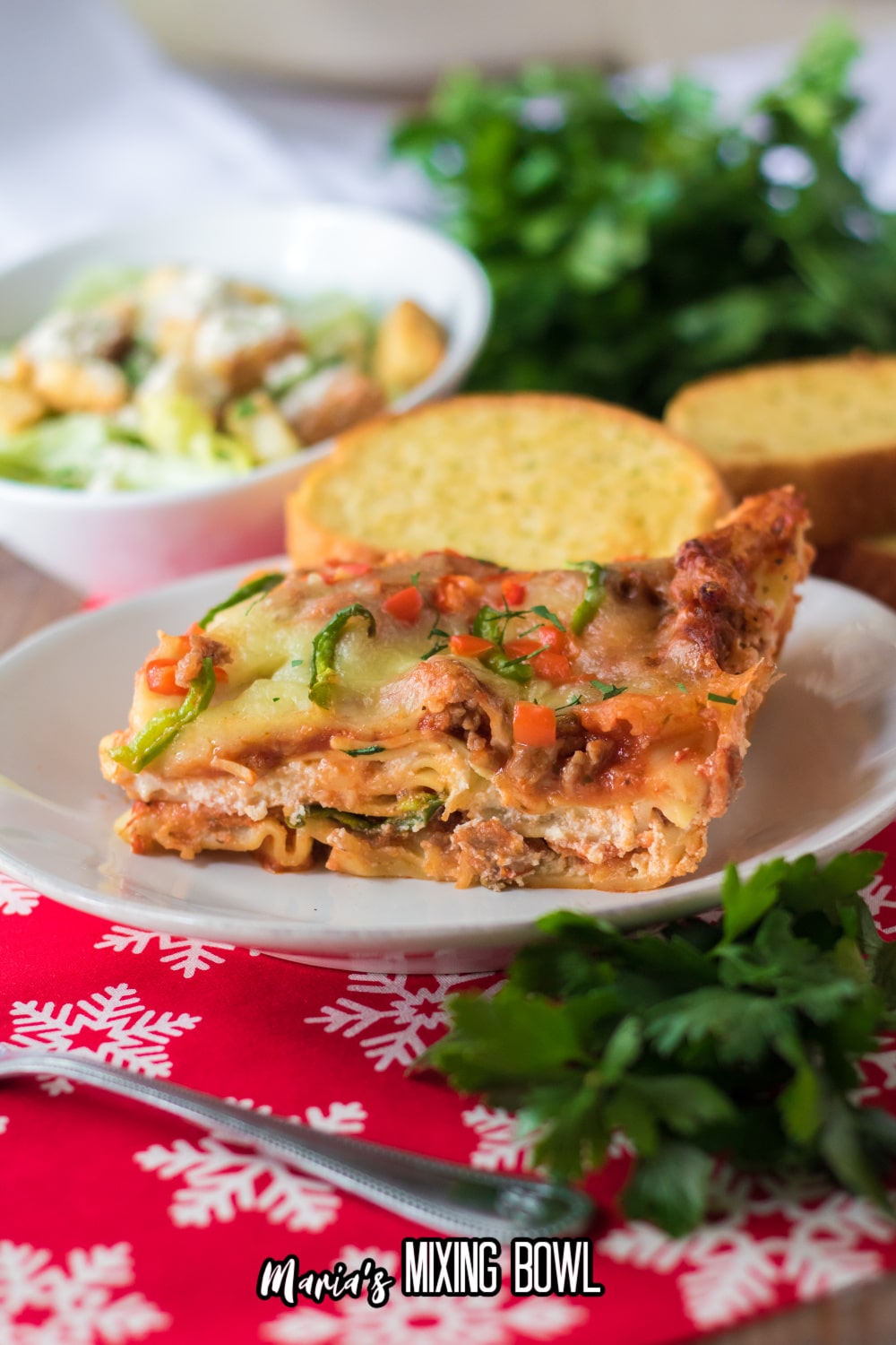 slice of christmas lasanga on a white plate with the a slice of garlic bread in the background