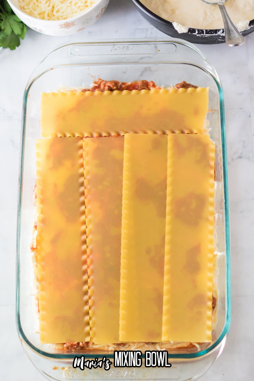 noodles, sauce and cheese being layered in a glass casserole dish