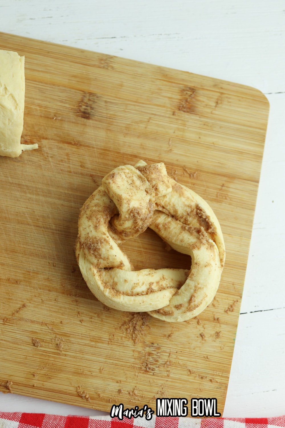raw cinnamon roll twisted into a wreath shape on a wooden cutting board