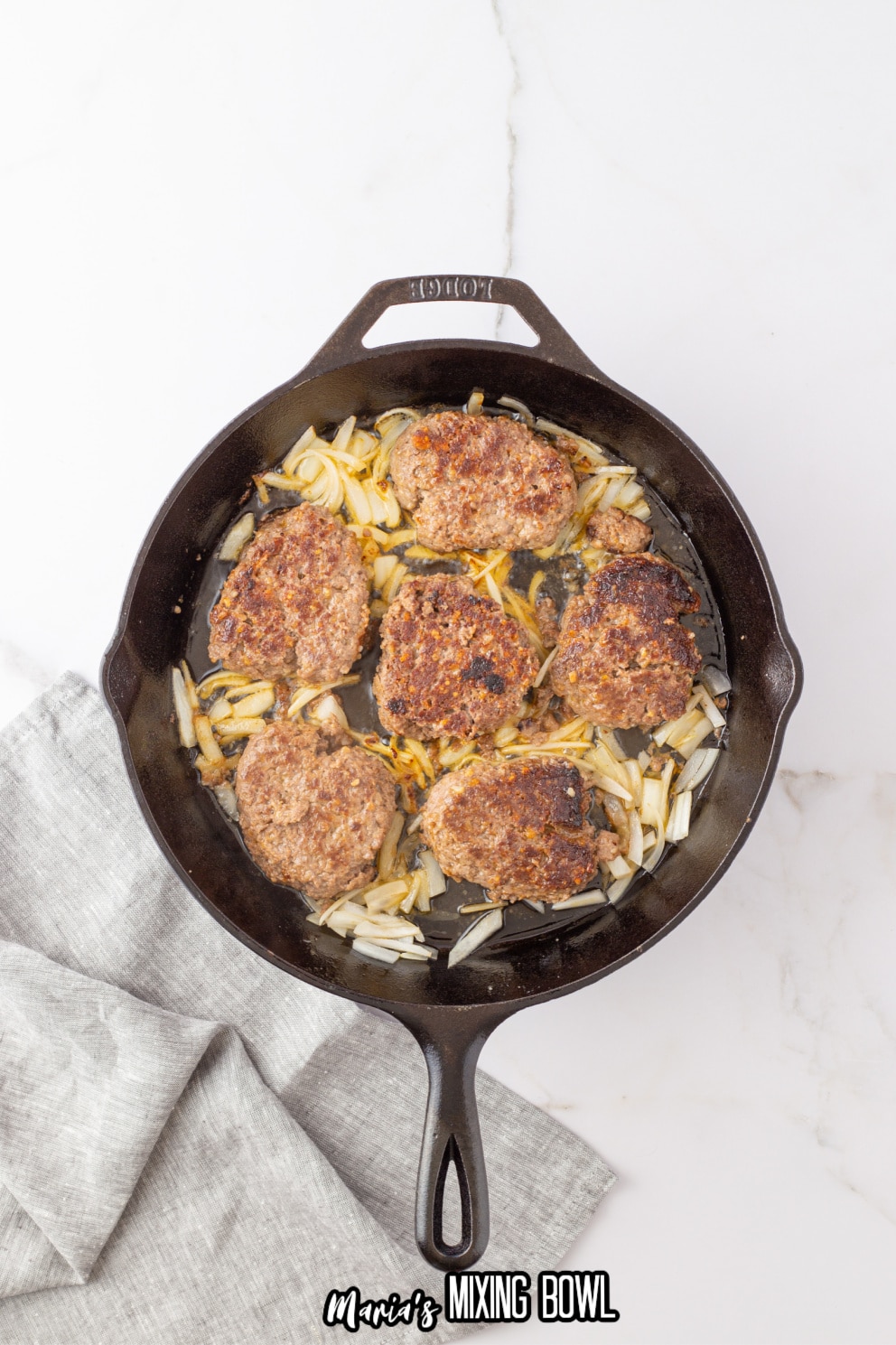 hamburger patties and onions in a cast iron skillet