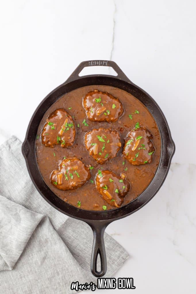 hamburger patties and onions in a cast iron skillet topped with brown gravy
