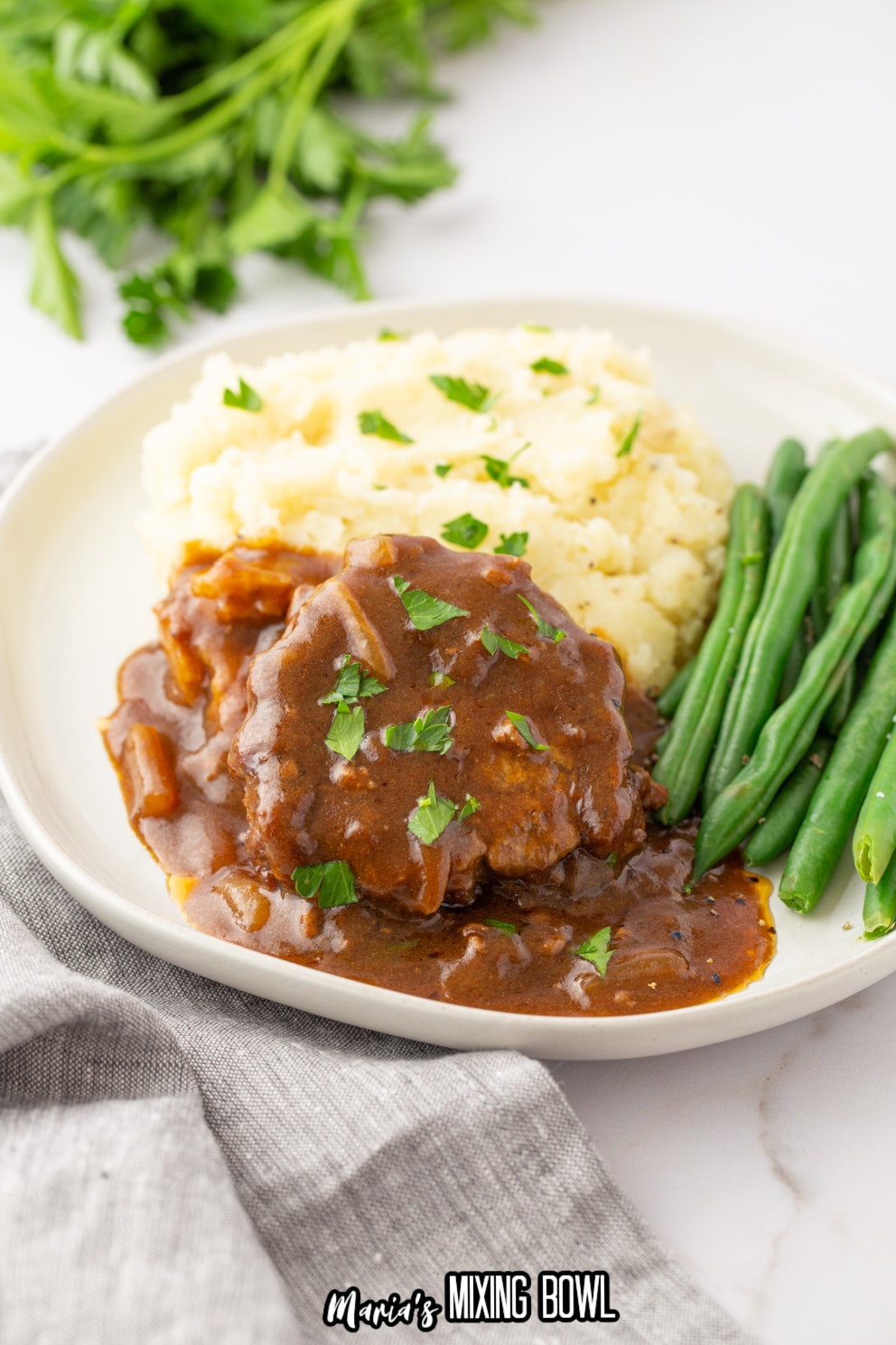 salisbury steaks with green beans and mashed potatoes on a white plate