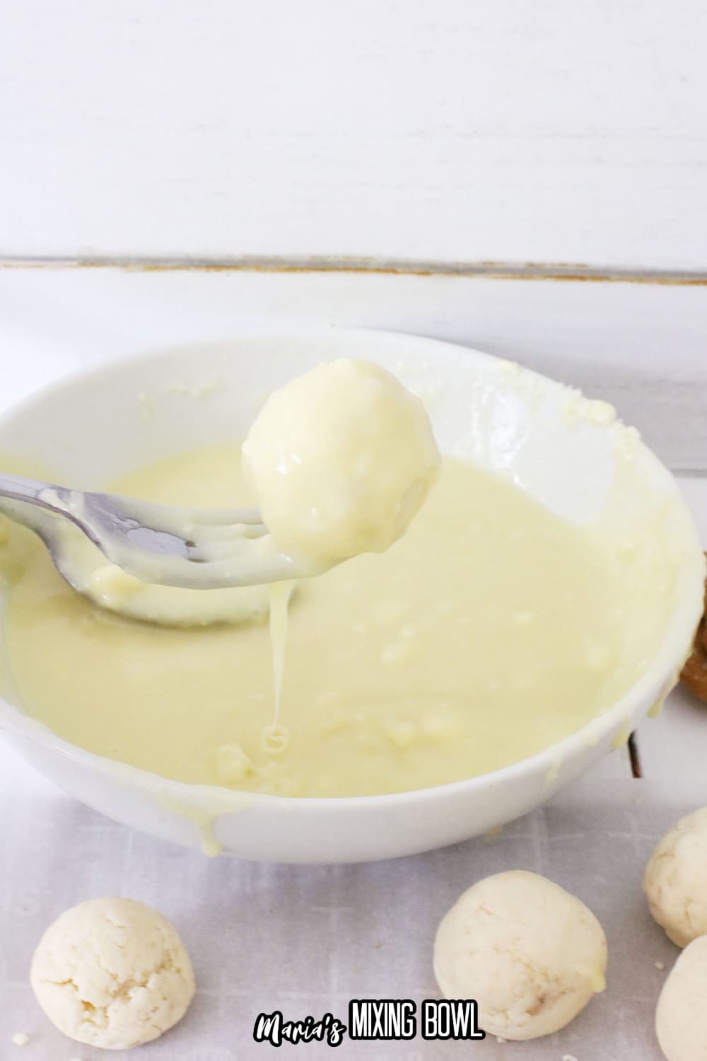 ball being dipped into melted white almond bark on a fork