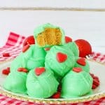 grinch peanut butter balls stacked on a white plate with gold rimmed edges