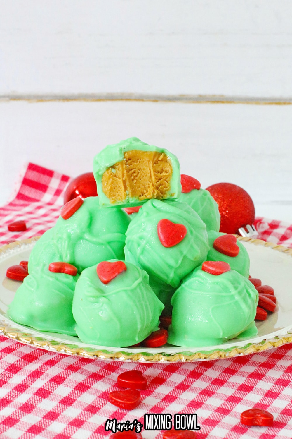 grinch peanut butter balls stacked on a white plate with gold rimmed edges