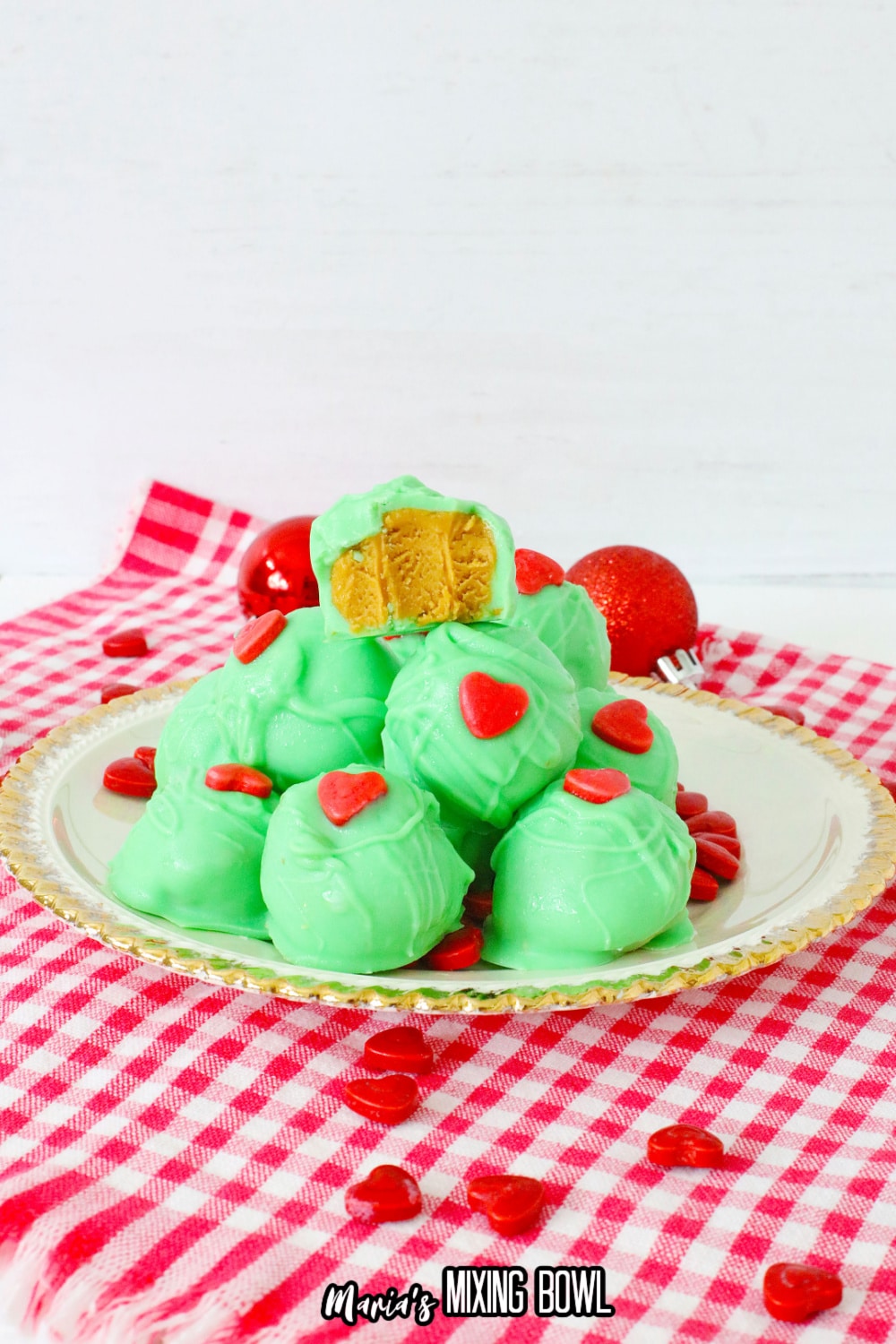 grinch peanut butter balls stacked on a white plate with gold rimmed edges