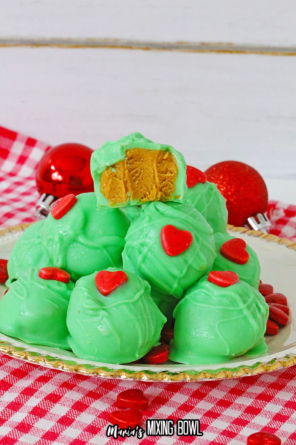 grinch peanut butter balls stacked on a white plate with gold rimmed edges