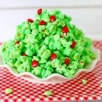 white plate on a red and white kitchen towel filled with grinch popcorn with the name in text for pinterest